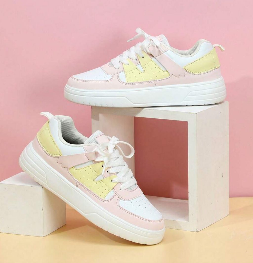 Baskets tendance blanches et roses avec détails jaunes, posées sur des cubes blancs, fond rose. Chaussures mode femme, style décontracté.