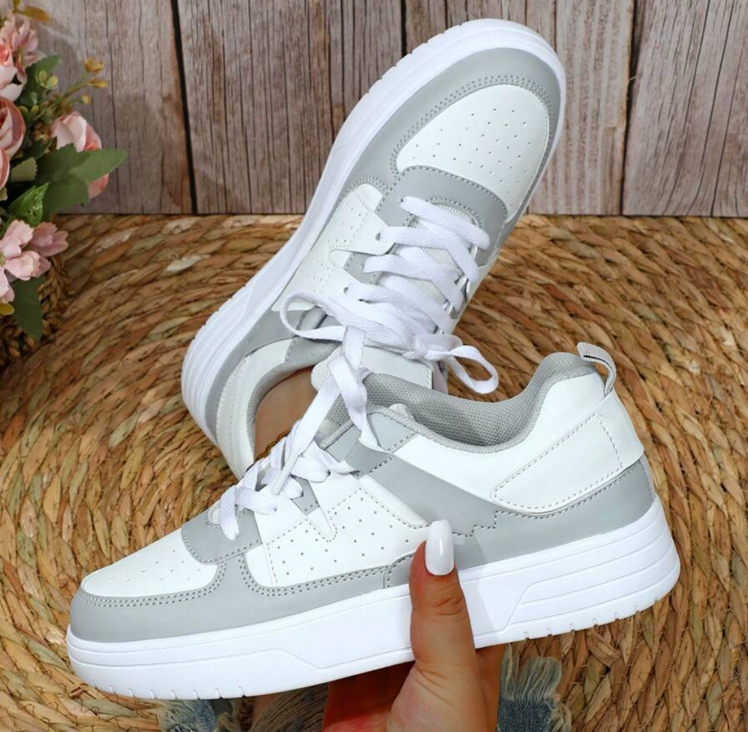 Chaussures de sport blanches et grises sur fond de bois, design moderne, lacets blancs, semelle épaisse. Idéales pour la mode urbaine et le confort.