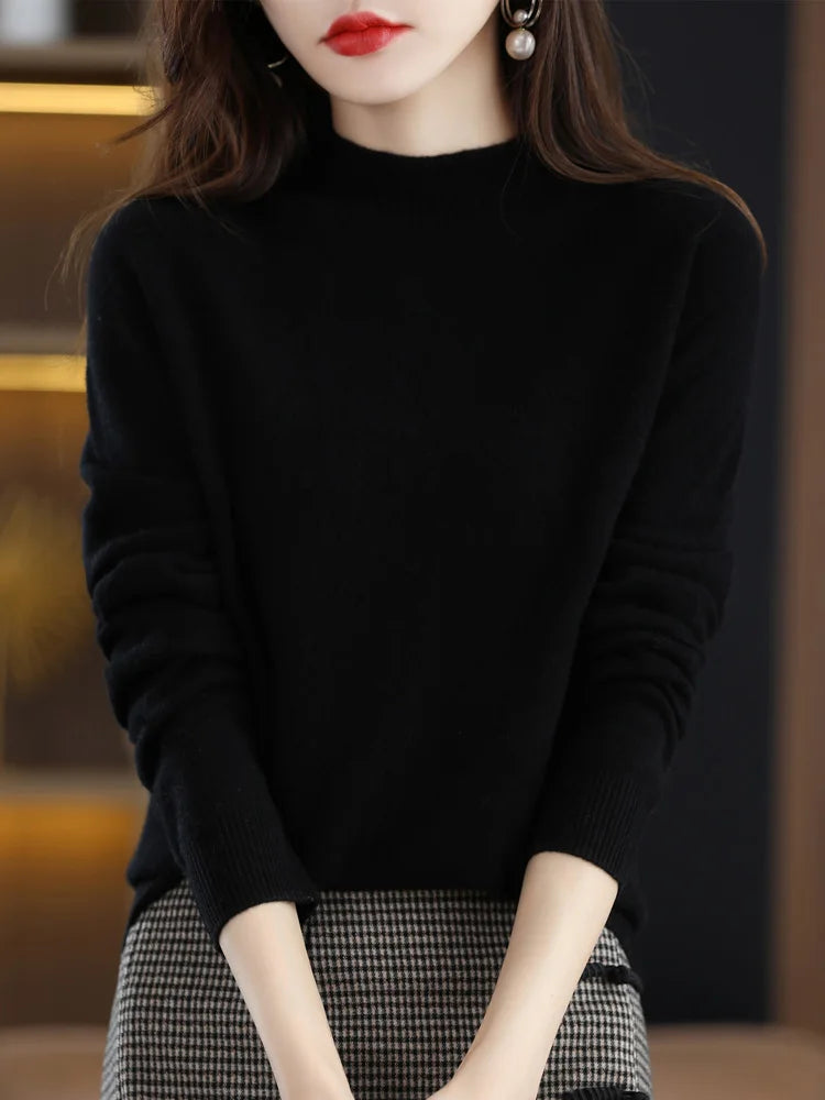Femme portant un pull noir élégant, manches longues, avec des boucles d'oreilles pendantes, posant dans un intérieur moderne. Mode automne-hiver chic.