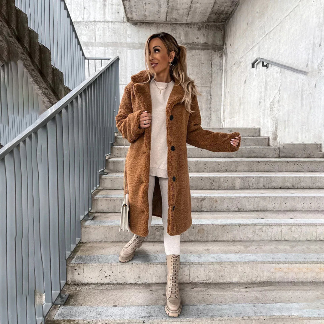 Femme en manteau en laine marron, tenue d'hiver élégante, escaliers en béton, bottes beiges, sac à main blanc, style urbain moderne.