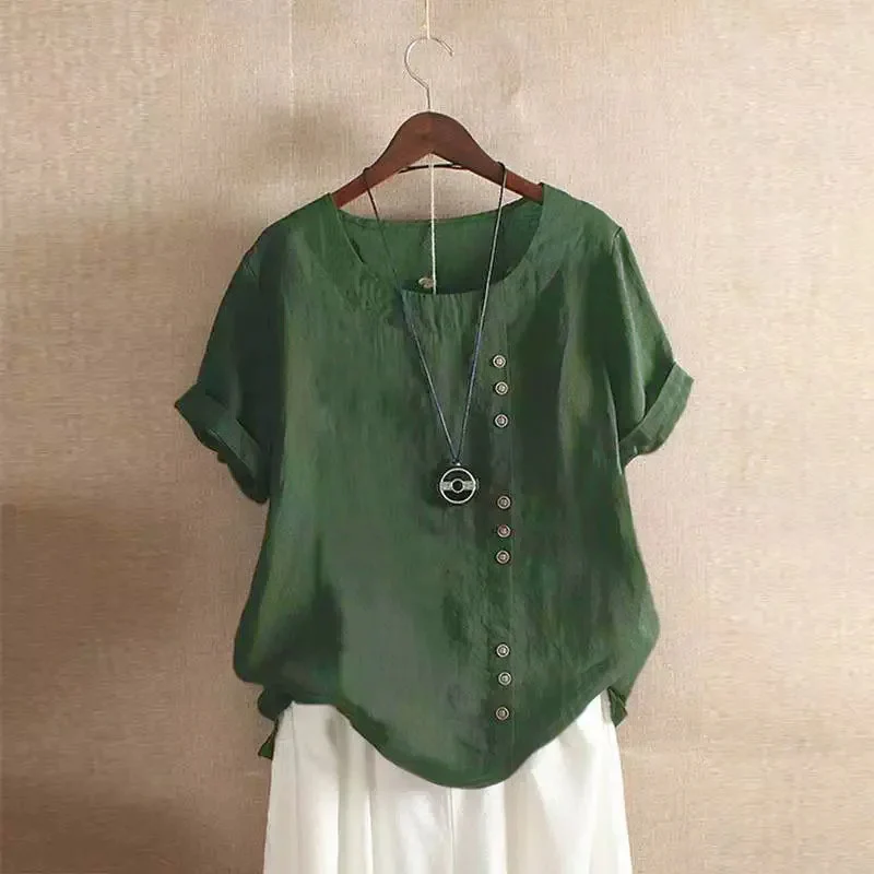 Blouse verte en lin avec boutons asymétriques, manches courtes retroussées, suspendue sur cintre en bois, fond beige. Mode éco-responsable.