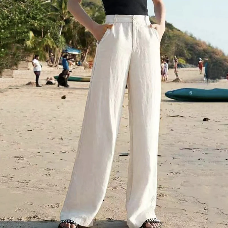 Personne portant un pantalon large blanc sur une plage ensoleillée, avec des palmiers en arrière-plan. Mode estivale, style décontracté, vacances.