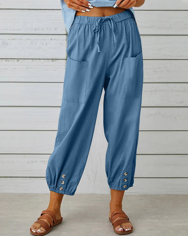 Pantalon ample bleu pour femme avec poches avant, taille élastique et boutons décoratifs aux chevilles, style décontracté estival.