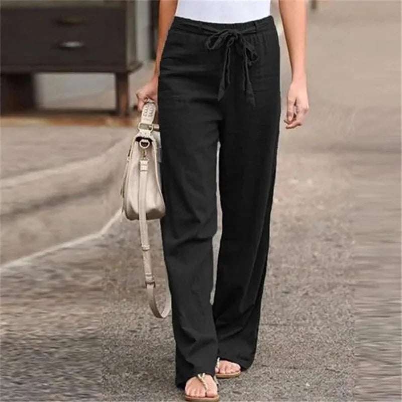 Pantalon noir ample pour femme, style décontracté, avec cordon à la taille, porté avec un sac à main beige et des sandales, mode urbaine.
