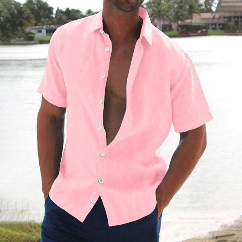 Homme portant une chemise rose ouverte devant un lac, style décontracté estival, mode masculine, chemise à manches courtes, paysage tropical.