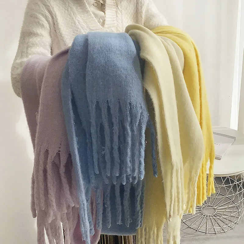 Écharpes en laine multicolores avec franges, tenues par une personne. Accessoires d'hiver tendance, doux et chauds, en bleu, jaune et lilas.
