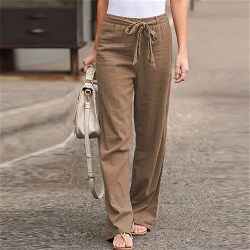 Pantalon en lin marron pour femme, taille haute avec cordon, porté avec un haut blanc et des sandales. Mode décontractée, style estival.