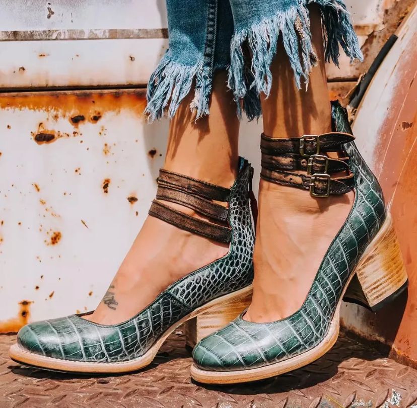 Chaussures à talons en cuir vert crocodile, avec brides marron à boucles, portées avec un jean effiloché. Mode tendance, style vintage.