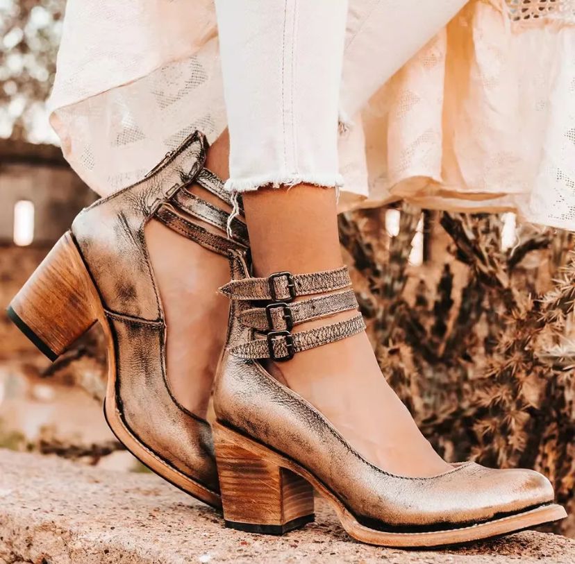 Chaussures à talons en cuir doré avec brides, portées avec un jean blanc et une robe en dentelle, posées sur un fond naturel.