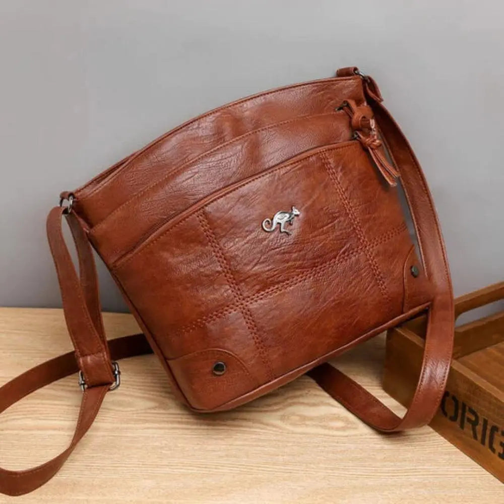 Sac à bandoulière en cuir marron, design élégant avec logo métallique, posé sur une table en bois. Accessoire mode femme tendance et pratique.