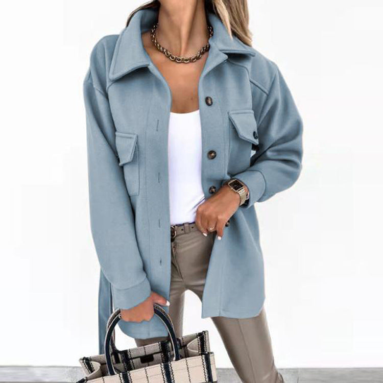 Femme portant une surchemise bleue élégante avec boutons, t-shirt blanc, pantalon beige, collier chaîne, sac à main à carreaux. Mode automne chic.