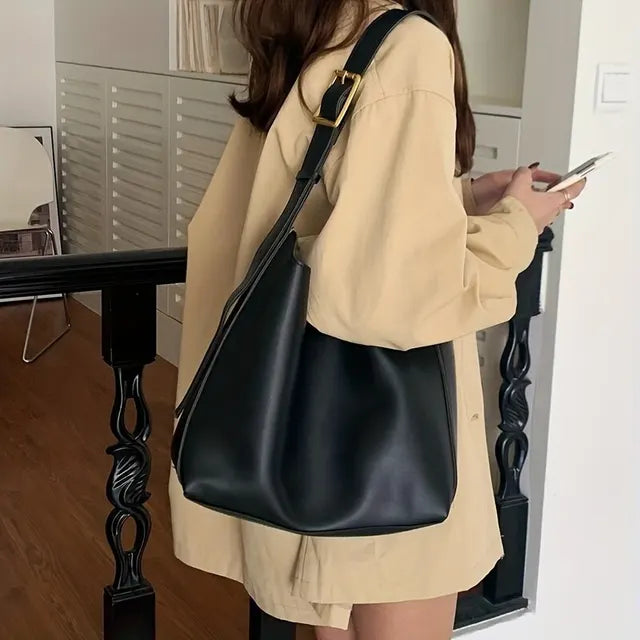Femme portant un grand sac à main noir en cuir, tenue beige, intérieur moderne. Mode féminine, accessoire tendance, style urbain chic.