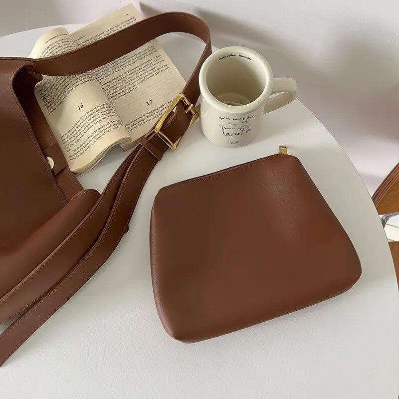 Sac à main en cuir marron avec pochette assortie sur table blanche, livre ouvert et tasse à café. Accessoires mode élégants et tendance.