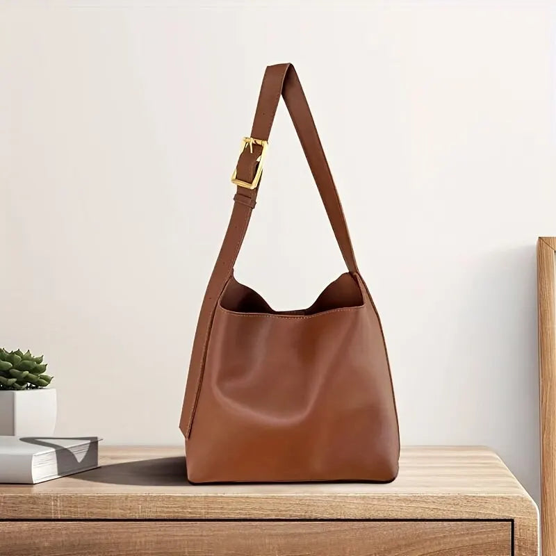 Sac à main en cuir marron sur une table en bois, avec une boucle dorée. Accessoire de mode élégant, parfait pour un style chic et moderne.