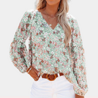 Blouse fleurie à manches longues, col en V, portée par une femme avec un pantalon blanc. Mode féminine, style décontracté, tendance printemps-été.