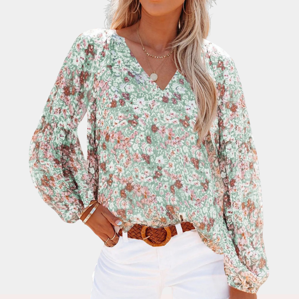 Blouse fleurie à manches longues, col en V, portée par une femme avec un pantalon blanc. Mode féminine, style décontracté, tendance printemps-été.