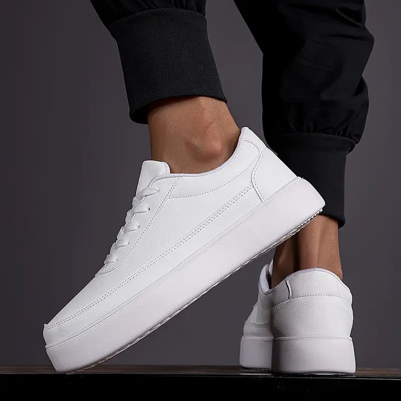 Chaussures blanches minimalistes pour homme, style décontracté, semelle épaisse, portées avec un pantalon noir. Mode urbaine tendance.