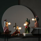 Quatre lampes décoratives en forme de personnages soufflant des bulles lumineuses, posées sur une table, créant une ambiance artistique et moderne.