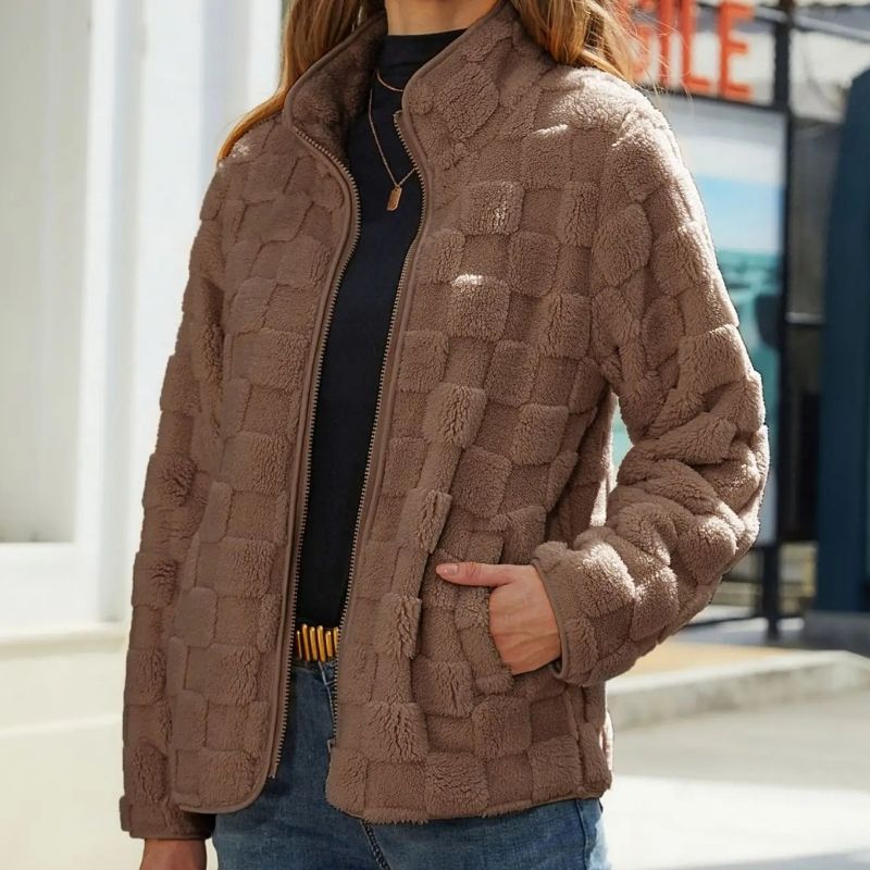 Veste en laine marron à motif damier, portée par une femme en extérieur. Mode automne-hiver, style décontracté, tendance vestimentaire féminine.