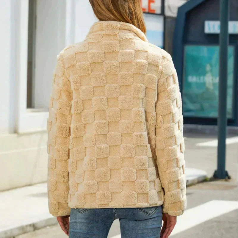 Veste en fausse fourrure beige à motif carré, vue de dos, portée par une femme en jean, dans une rue urbaine. Mode automne-hiver tendance.