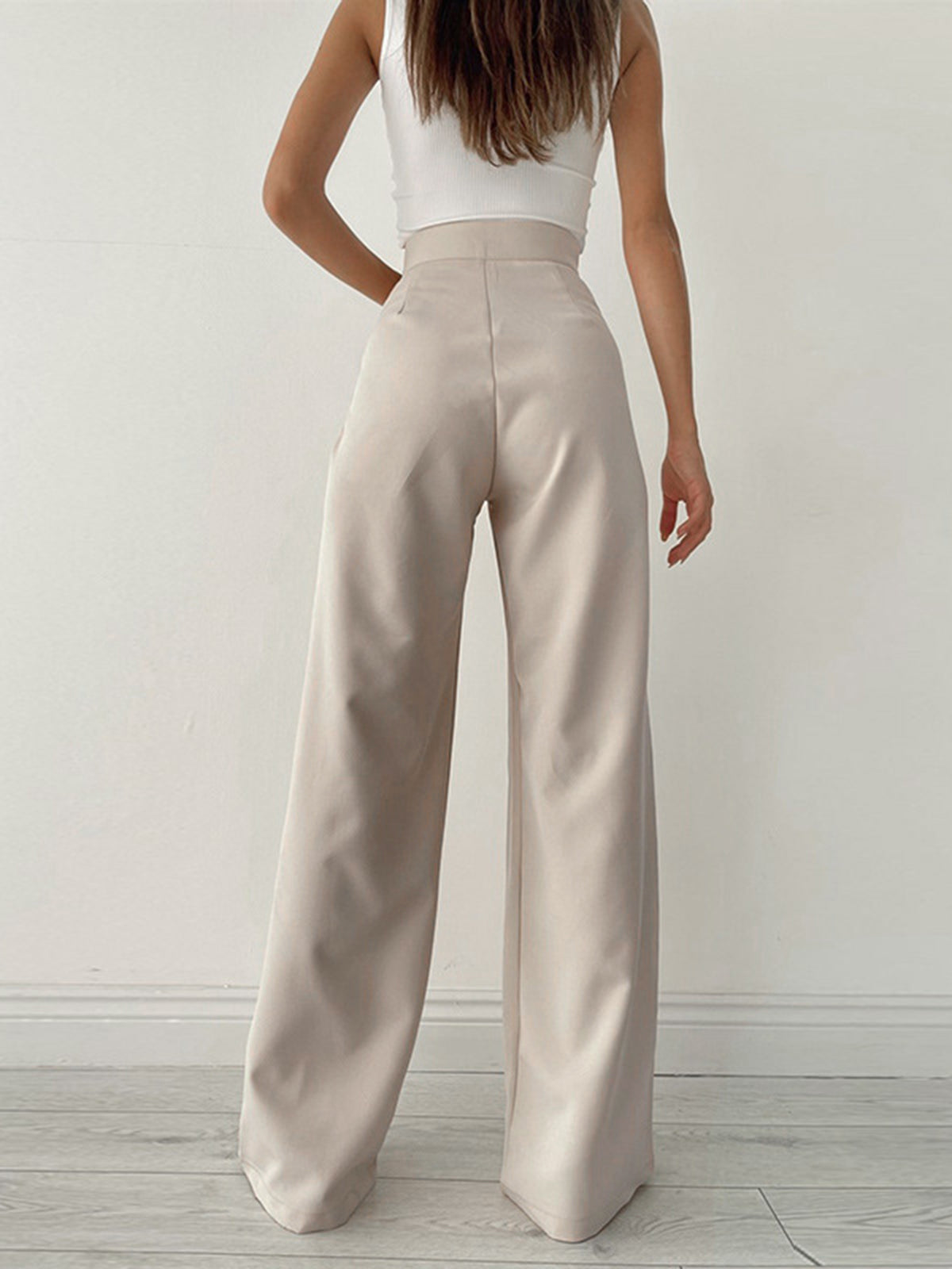 Femme portant un pantalon large beige taille haute, vue de dos, sur fond blanc. Mode féminine élégante, tendance minimaliste, style décontracté.