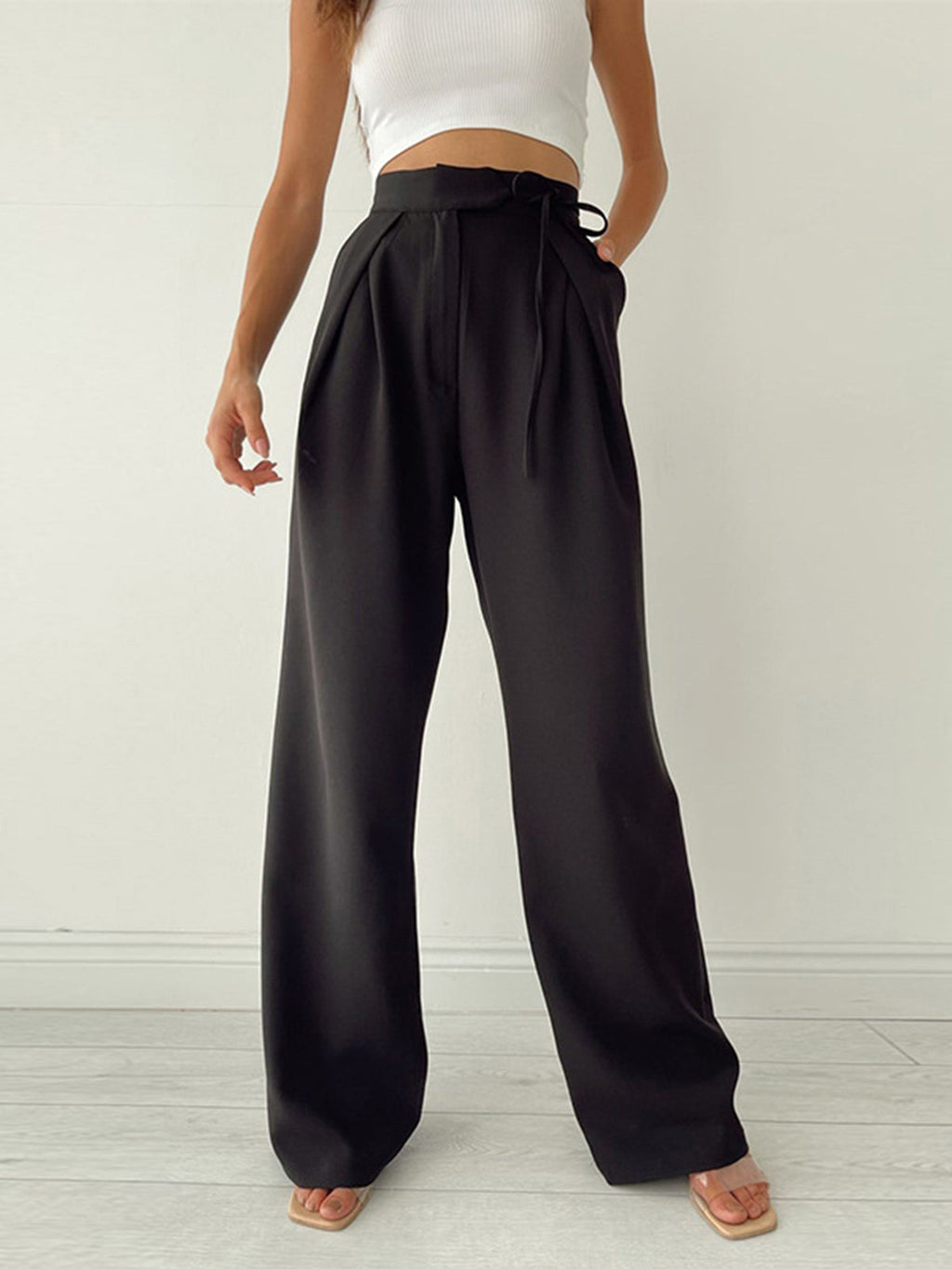 Femme portant un pantalon noir taille haute, ample, avec un haut blanc sans manches. Mode élégante et décontractée, tendance vêtements féminins.