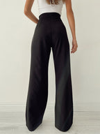 Femme portant un pantalon large noir taille haute, vue de dos, avec un haut blanc sans manches. Mode élégante et moderne, style minimaliste.
