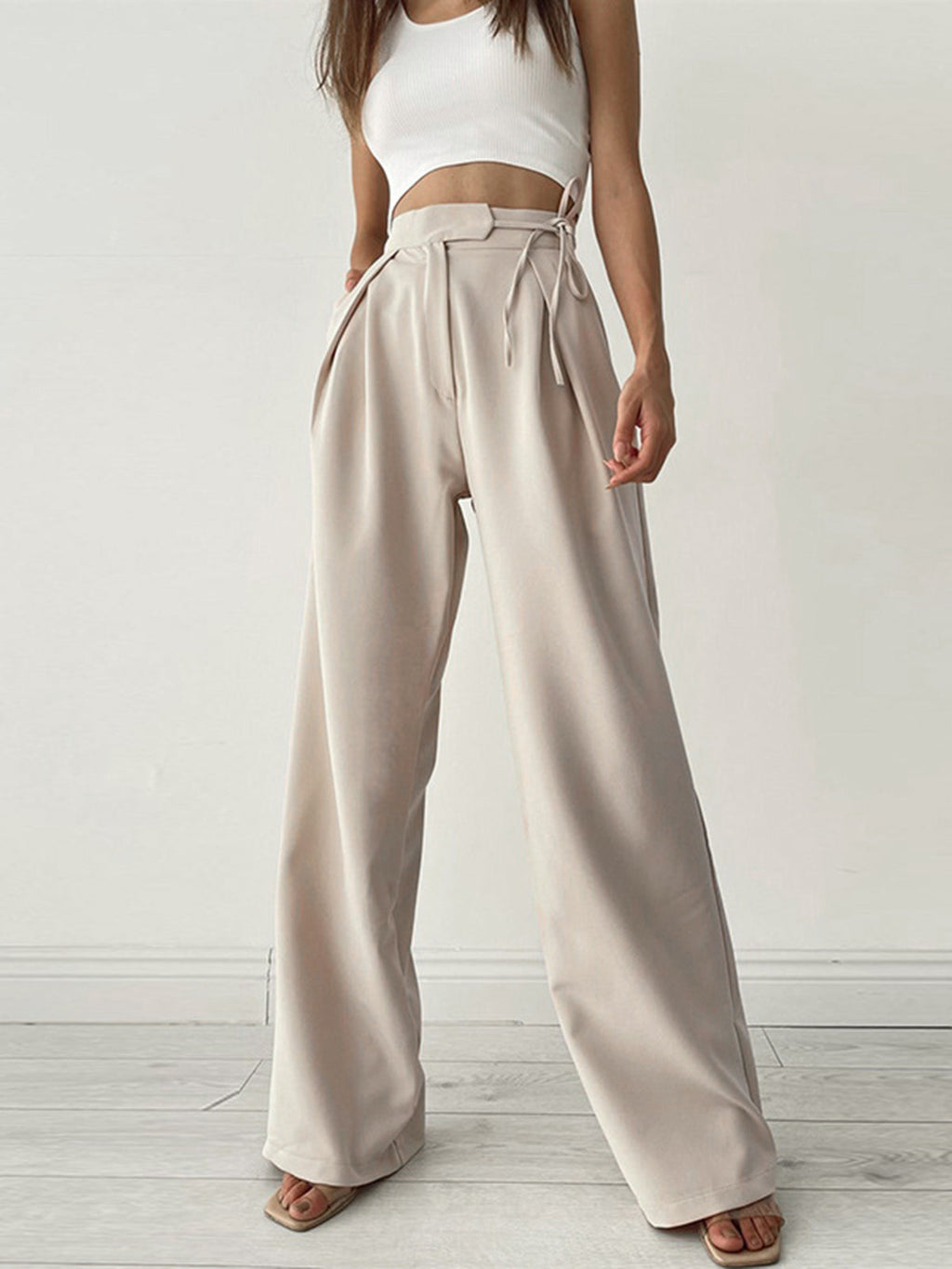 Femme portant un pantalon large beige taille haute avec un top blanc court, mode décontractée, style moderne, intérieur minimaliste.