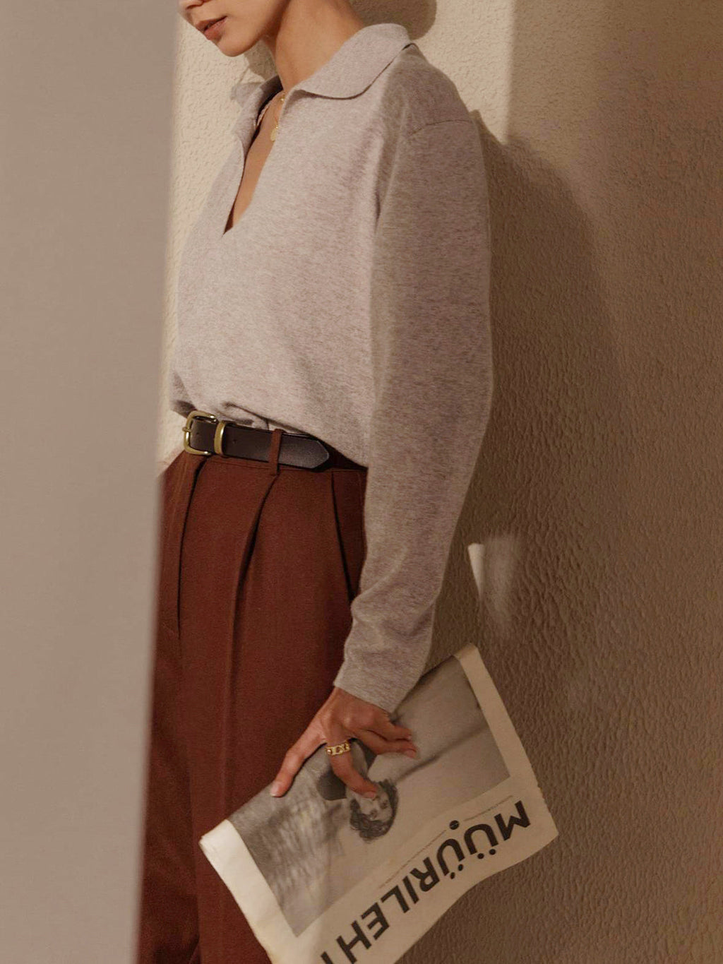 Femme élégante en pull gris et pantalon marron, tenant un magazine. Mode automne, style chic, tenue décontractée, accessoires minimalistes.