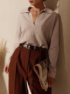 Femme élégante portant un pull beige à col ouvert et un pantalon marron, tenant un journal. Mode automne chic, style décontracté sophistiqué.