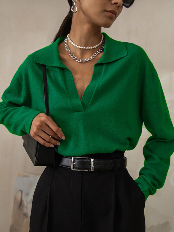 Femme portant un pull vert vif avec col en V, collier en chaîne argentée, pantalon noir taille haute et sac à bandoulière noir. Mode élégante et moderne.