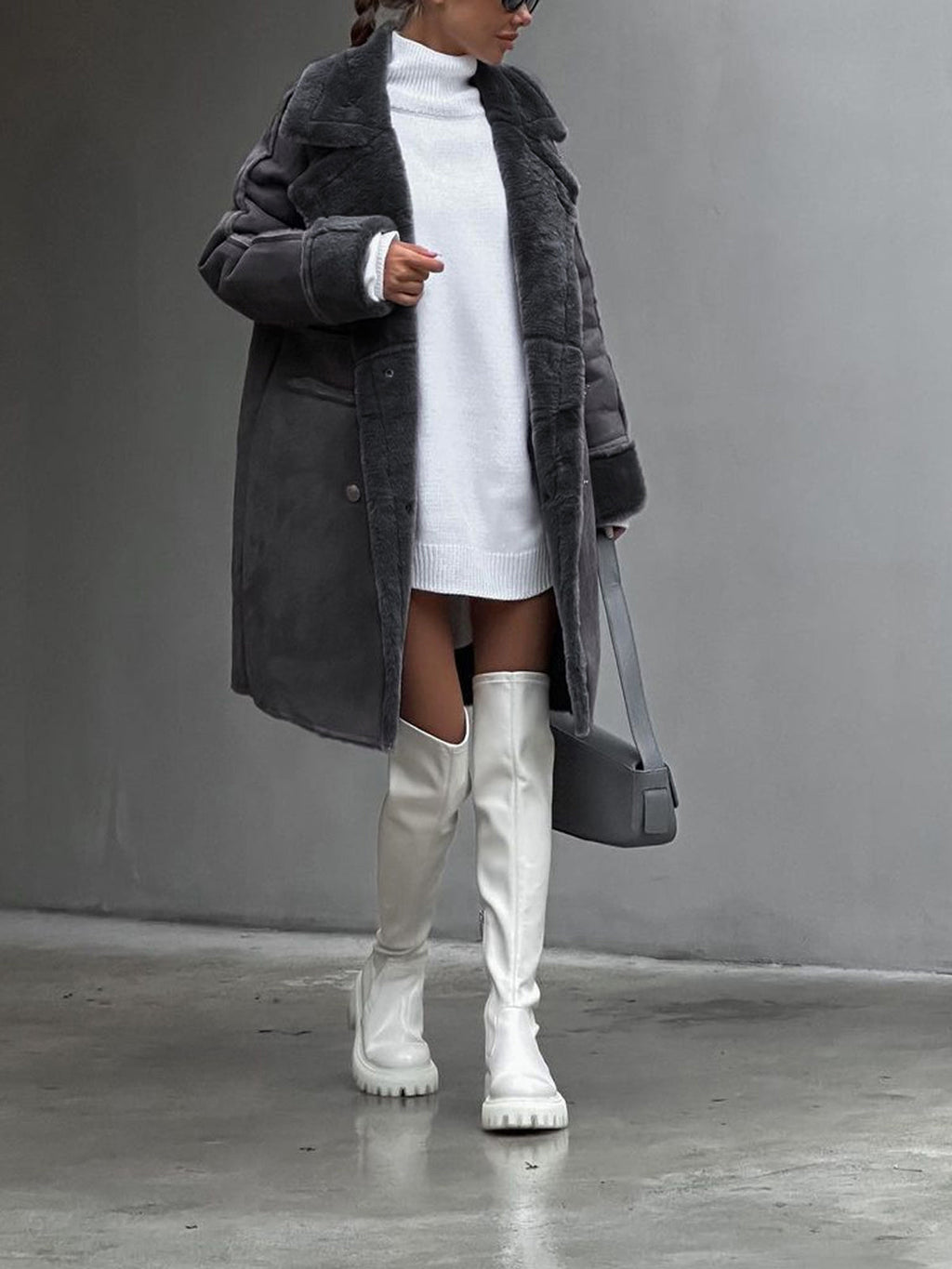 Femme en manteau gris et robe pull blanche, portant des cuissardes blanches et un sac à main gris. Mode hiver élégante et moderne.
