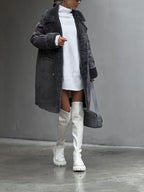 Femme en manteau gris et robe pull blanche, portant des cuissardes blanches et un sac à main gris. Mode hiver élégante et moderne.