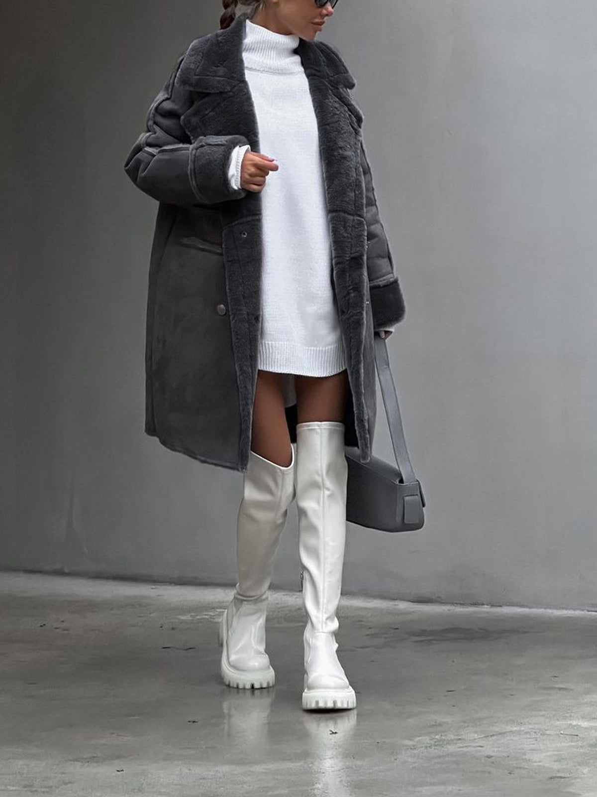 Femme en manteau gris et robe pull blanche, portant des cuissardes blanches et un sac à main gris. Mode hiver élégante et moderne.