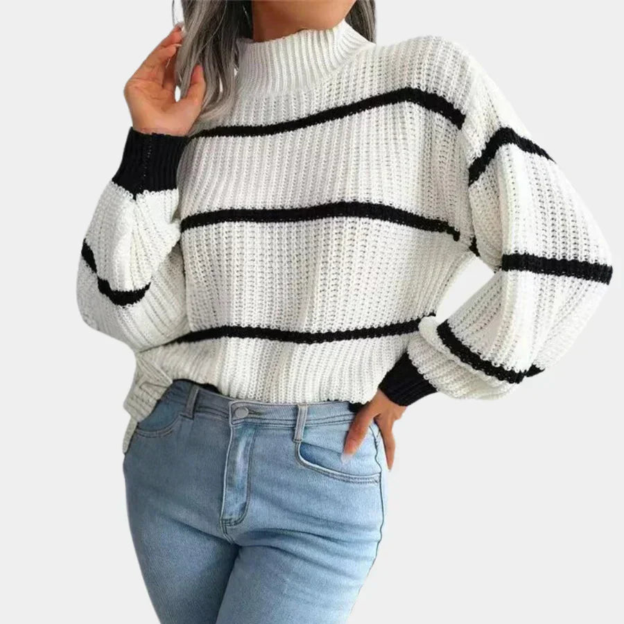 Femme portant un pull en maille blanc à rayures noires, manches longues, col montant, associé à un jean bleu clair. Mode automne-hiver tendance.