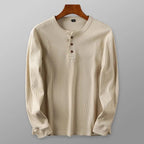 Chemise henley beige à manches longues, col rond, trois boutons en bois, suspendue sur un cintre en bois. Mode homme, style décontracté.