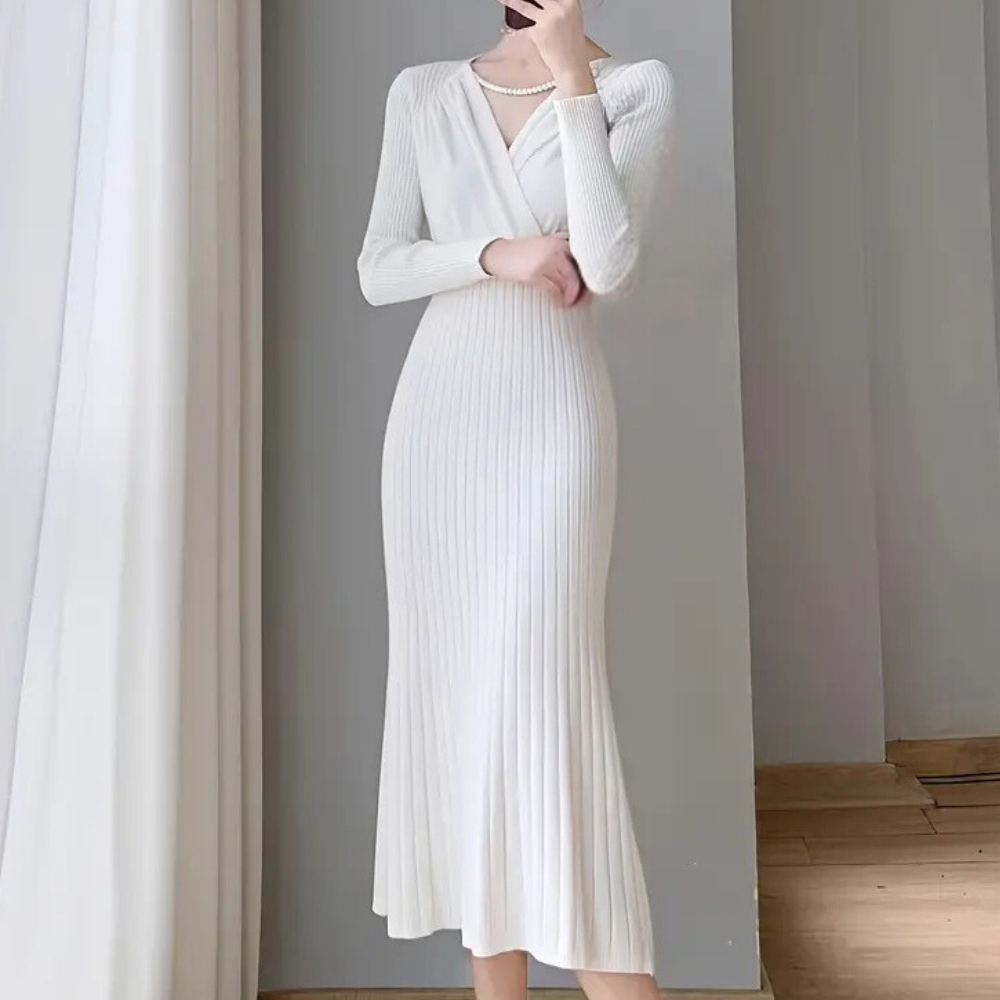 Robe longue blanche élégante en tricot côtelé, manches longues, col en V croisé, portée par une femme, style chic et moderne, intérieur minimaliste.