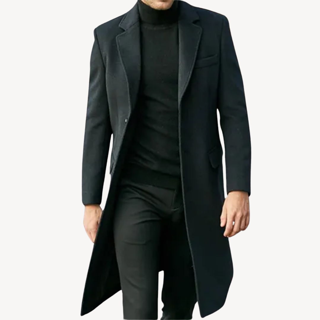 Manteau long noir élégant pour homme, style classique, porté avec un pull noir et un pantalon assorti. Mode masculine chic et intemporelle.