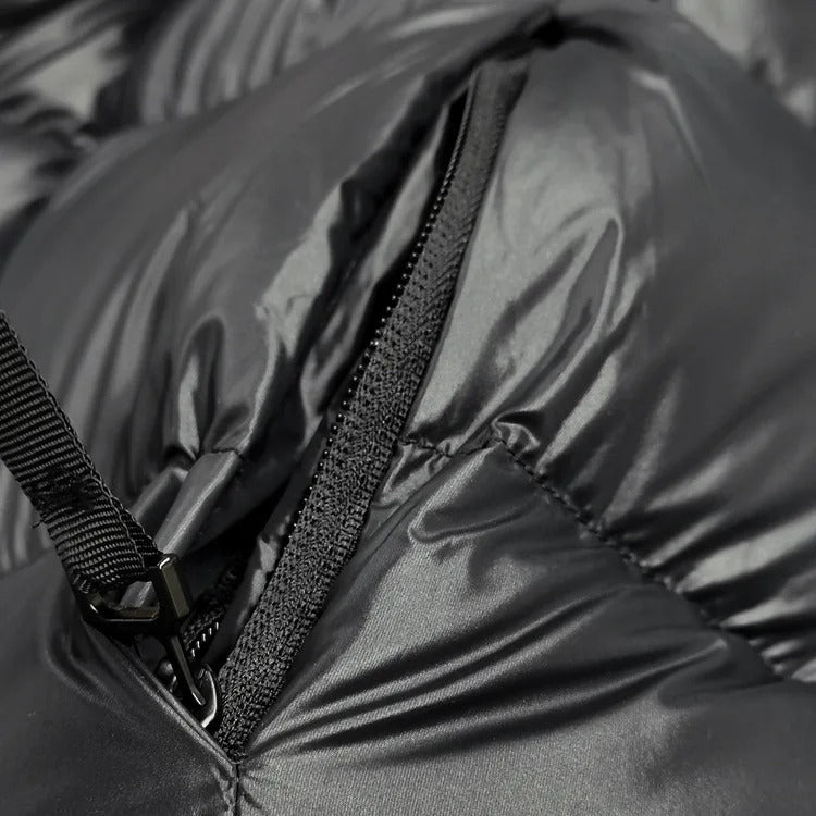 Gros plan d'une doudoune noire avec fermeture éclair, tissu brillant et texture matelassée. Mode hiver, vêtement chaud, tendance.