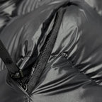 Gros plan d'une doudoune noire avec fermeture éclair, tissu brillant et texture matelassée. Mode hiver, vêtement chaud, tendance.