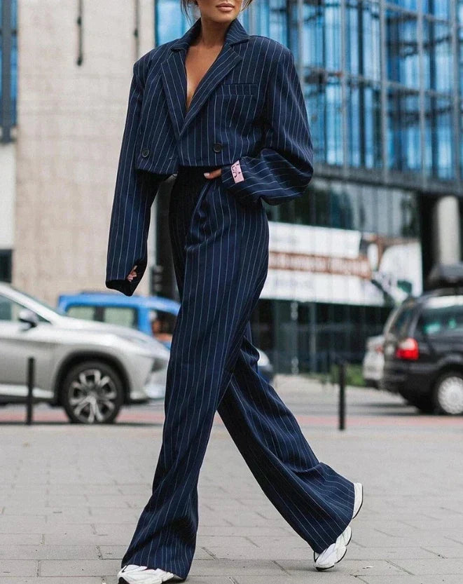 Femme portant un costume bleu marine à rayures, veste courte et pantalon large, marchant en ville. Mode urbaine élégante, tendance automne.