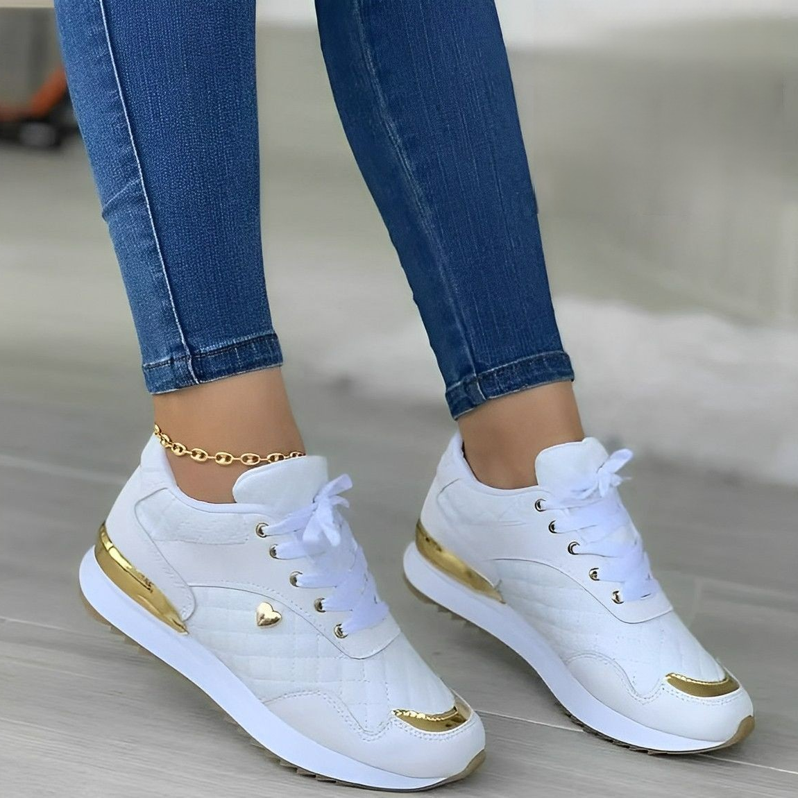 Baskets blanches et dorées pour femme, portées avec un jean bleu. Chaussures de sport élégantes, tendance, avec détails métalliques.
