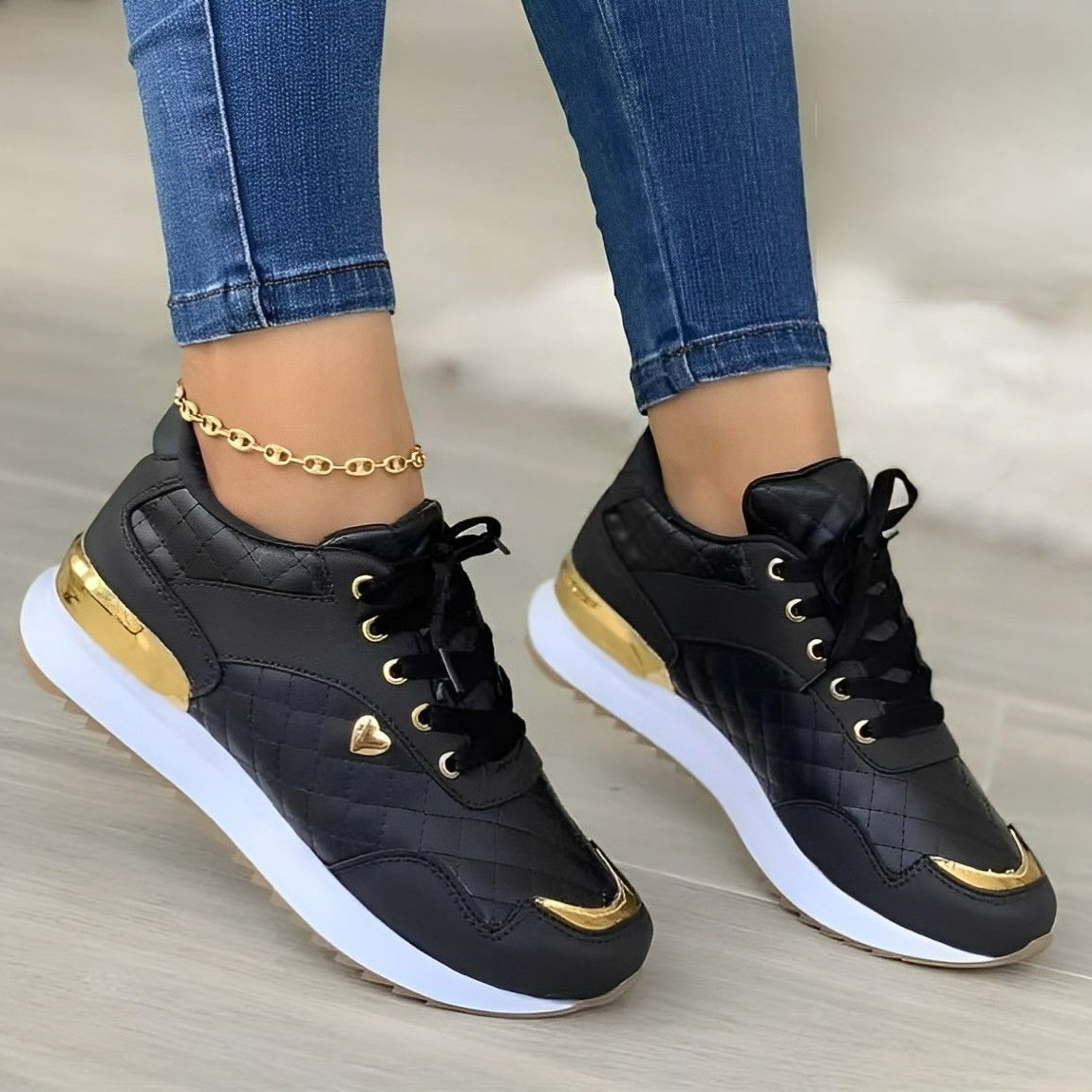 Chaussures de sport noires et dorées pour femme, avec détails en cuir matelassé, portées avec un jean ajusté. Sneakers tendance et élégantes.