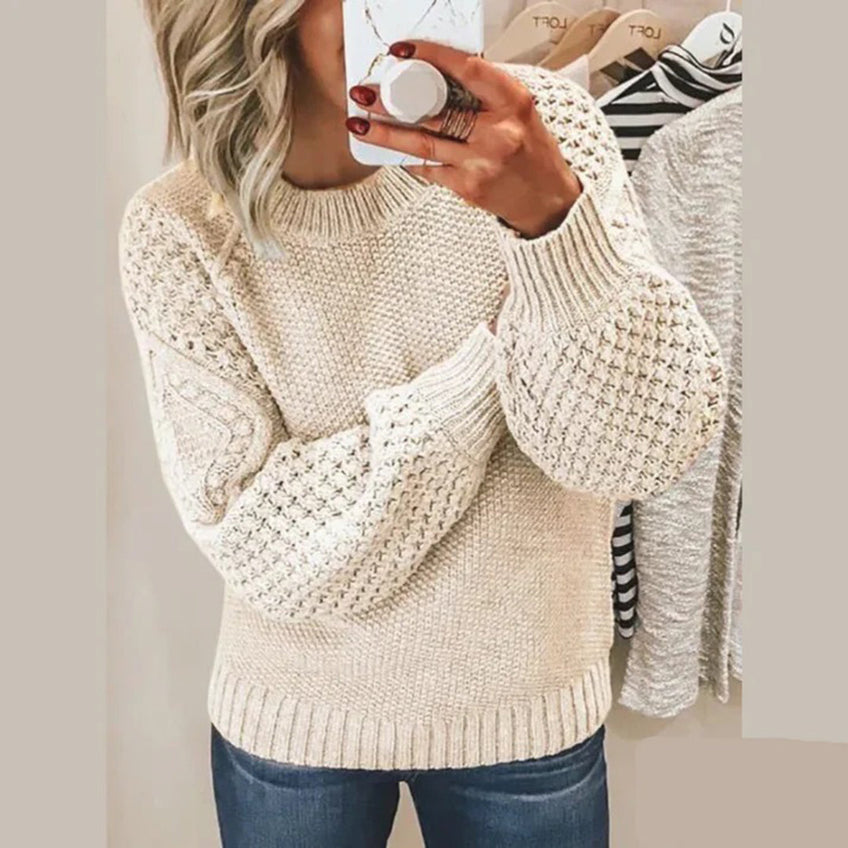 Femme portant un pull en tricot beige avec manches texturées, tenant un smartphone devant un miroir. Mode automne, style décontracté, tendance 2023.