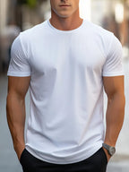 Homme portant un t-shirt blanc ajusté, manches courtes, dans une rue urbaine. Mode masculine, style décontracté, tenue estivale.