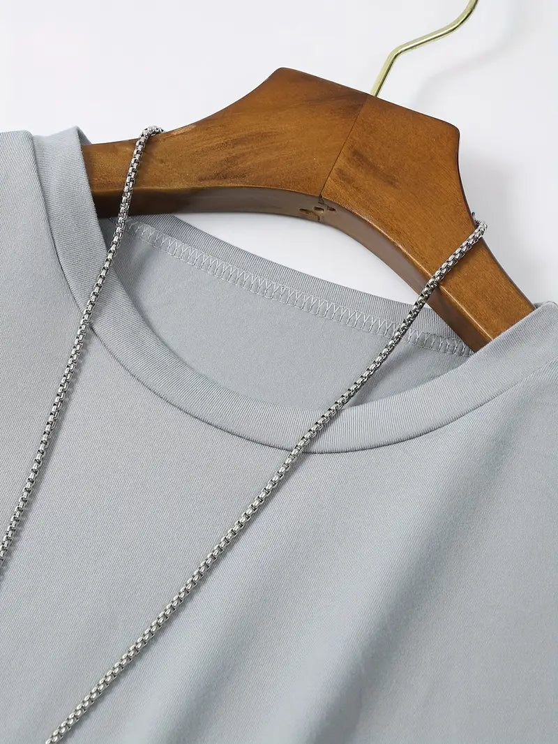 T-shirt gris en coton sur cintre en bois, chaîne argentée. Mode décontractée, vêtement basique, style minimaliste.