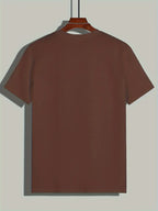 T-shirt marron uni suspendu sur un cintre en bois, fond gris. Mode décontractée, vêtement basique, style minimaliste, prêt-à-porter.