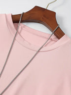 T-shirt rose en coton sur cintre en bois, chaîne argentée posée dessus, mode féminine, vêtement décontracté, style minimaliste.
