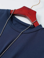 T-shirt bleu marine en polyester sur cintre en bois rouge, avec chaîne argentée. Mode homme, vêtement décontracté, style moderne.
