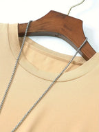 T-shirt beige en coton sur cintre en bois, avec chaîne argentée. Mode décontractée, vêtement basique, style minimaliste.